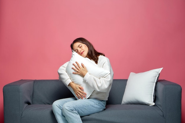 Calm beautiful young girl embracing pillow with closed eyes relaxing resting feeling sleepy sitting