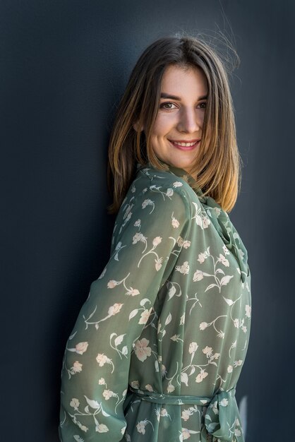 Calm beautiful young woman in elegant green dress near black wall. Fashion female portrait