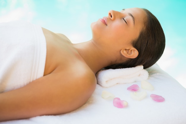 Calm brunette lying on towel with rose petals