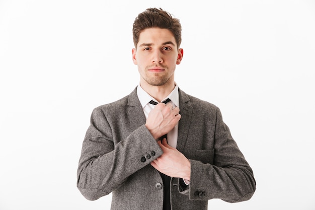 Calm business man in jacket corrects his tie  over white wall