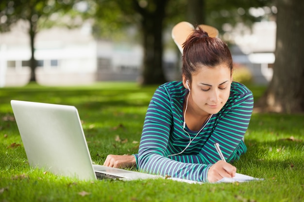 Studente casual calmo sdraiato sull'erba a prendere appunti