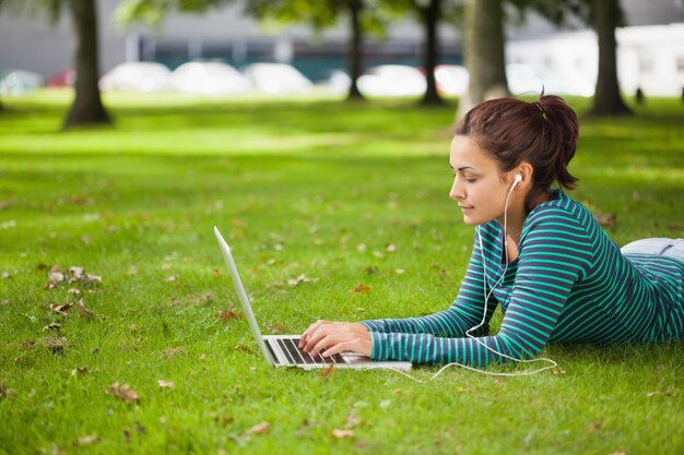 Calm casual student lying on grass using laptop