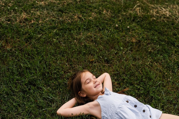 穏やかな子供の女の子が目を閉じて草の上に横たわり、草の上でリラックスした幸せな幼児の子供のライフスタイルを楽しんでください