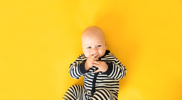 Photo calm curious baby lying on yellow background, looking at camera, top view, copy space