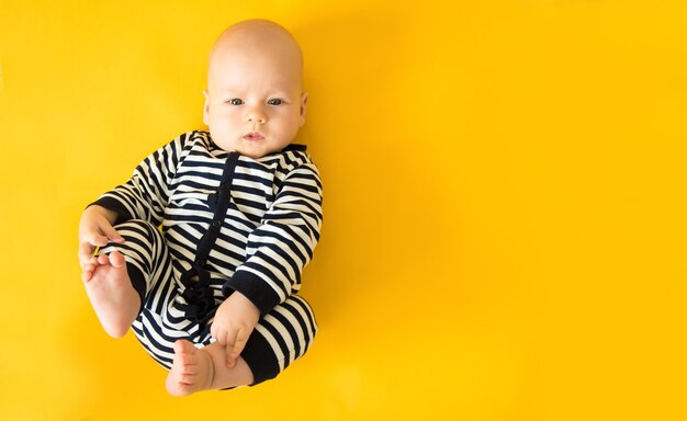 Photo calm curious baby lying on yellow background, , top view, copy space