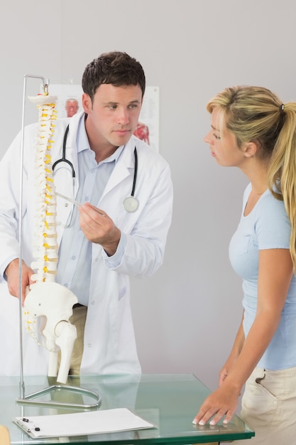 Calm doctor showing a patient something on skeleton model