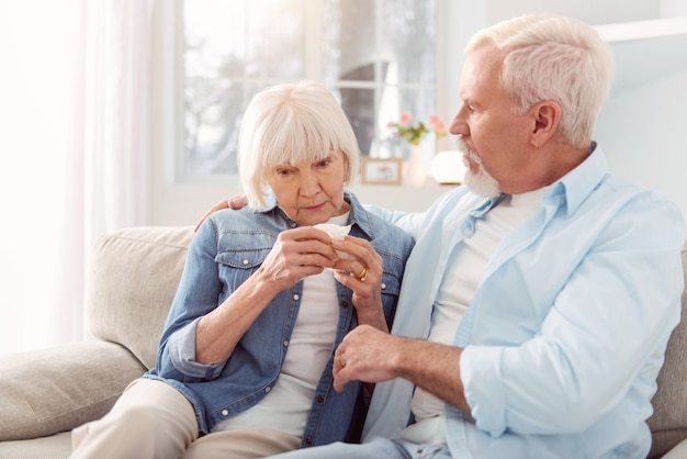 Calm down. Loving senior man sitting on the couch next to his wife, hugging and consoling her while she crying having heard bad news