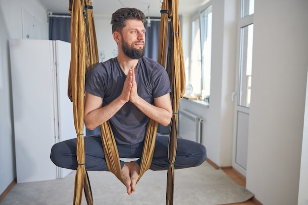 Calm dreamy male with his hands clasped sitting in a lotus pose in a hammock