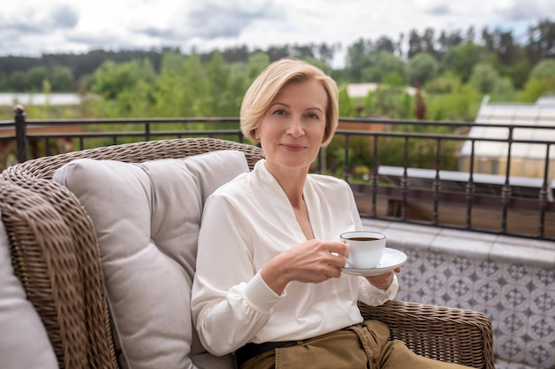 Calm elegant blonde woman drinking coffee outdoors