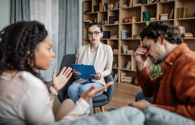 Photo calm european millennial female psychologist consults quarreling multiracial husband and wife