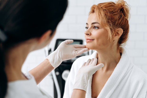 Foto cliente femminile calma soddisfatta del risultato dopo la procedura cosmetica. bella donna seduta sul divano davanti al dottore, mentre esamina la sua pelle. concetto di bellezza e cura della pelle