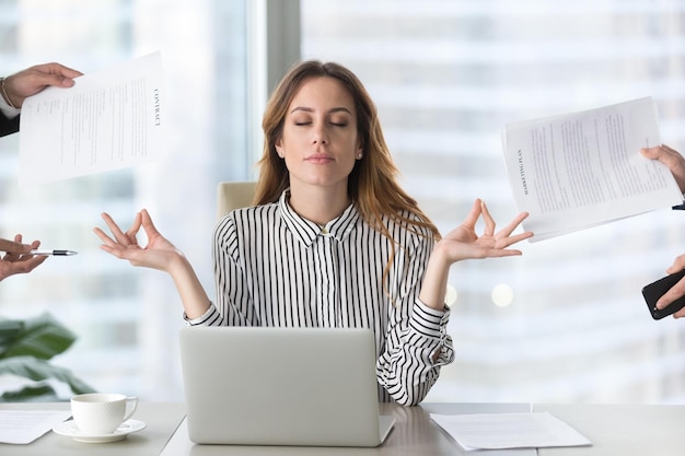 Foto calma dirigente femminile meditando prendendo una pausa al lavoro per l'equilibrio mentale donna d'affari consapevole sensazione di sollievo e senza stress facendo yoga al lavoro ignorando evitando lavoro stressante e scartoffie in ufficio