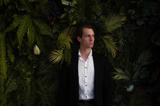 Спокойный фронтальный портрет мужчины в деловом костюме на фоне стены растений, папоротников и пальм.