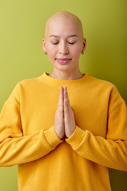 Calm and gorgeous young bald woman with closed eyes posing at camera, praying.