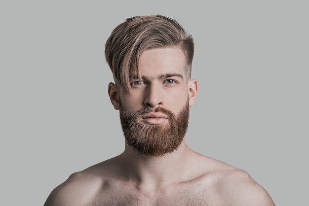 Calm and handsome. Portrait of young handsome man looking at camera while standing against grey background