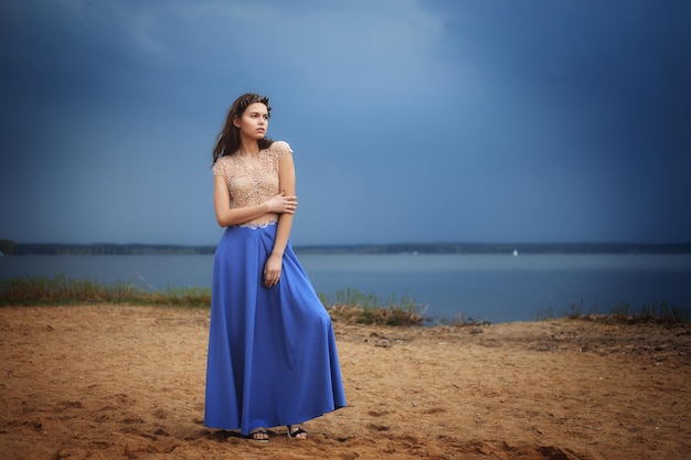 Calm lonely fashion model standing on a beach in a cloudy day