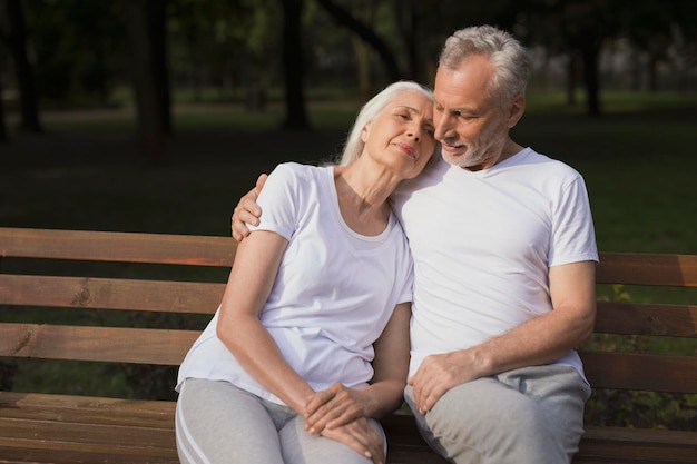 Calm mature lady relaxing with husband on a bench in the park