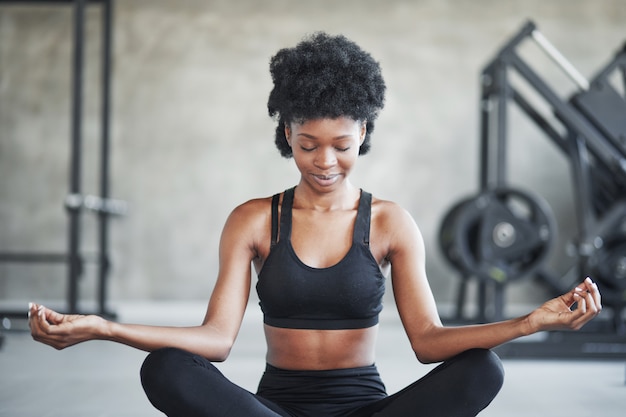Calm mind. African american woman with curly hair and in sportive clothes have fitness day in the gym
