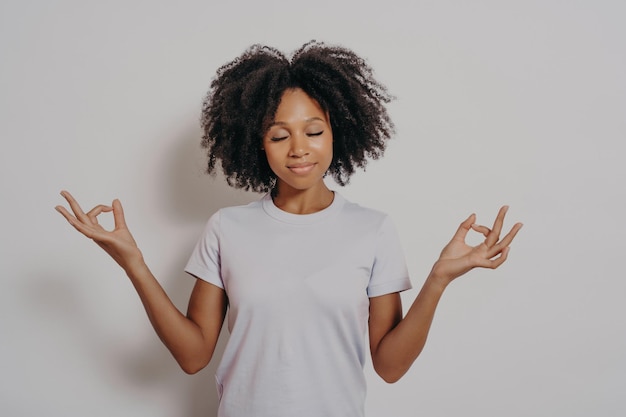 Calma e pacifica giovane donna di razza mista che tiene le mani nel gesto mudra e gli occhi chiusi