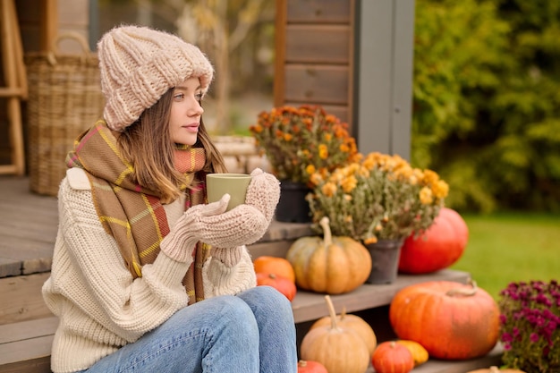 Calm pensive young woman sitting on the wooden porch steps and looking into the distance