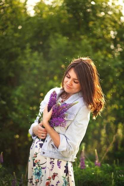 Foto ritratto calmo di una ragazza sognante femminile con gli occhi chiusi che abbraccia un mazzo di lupini viola