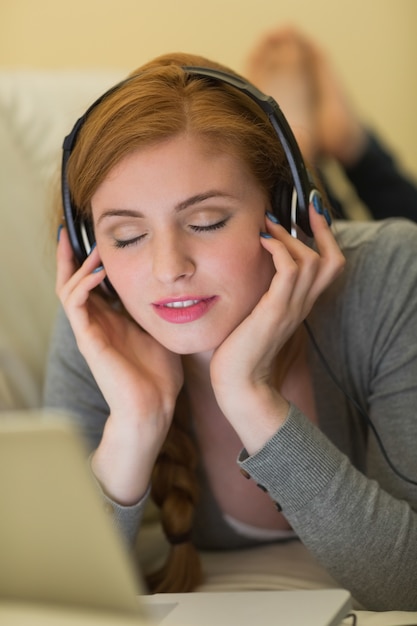 Calm redhead lying on the sofa with her laptop listening to music