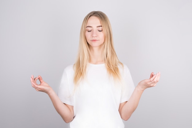 Calma, rilassata, una bella bionda allevia lo stress, chiude gli occhi e sorride pacificamente, meditando