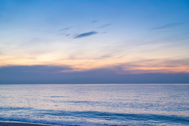 夕焼けの空と太陽と海と空の背景の雲の向こうの穏やかな海静かな海の景色水面の地平線色とりどりの雲とオレンジ色の日光の夕方の海の夕焼け空