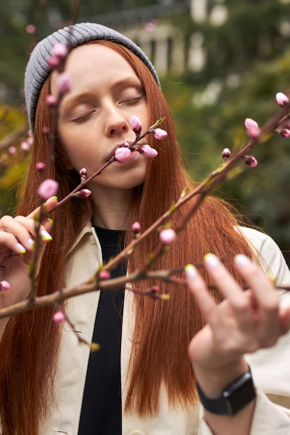 Calm sensual redhead female inhale the smell of blooming magnolia tree touching tree branches standi...