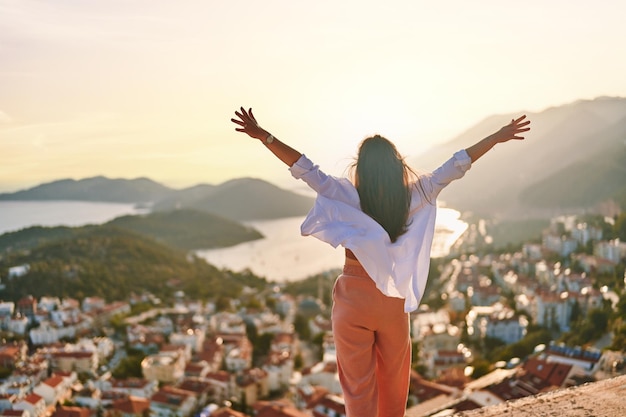 Calm serene happy inspired female stands alone with open arms and looks into the distance at beautiful view at sunset