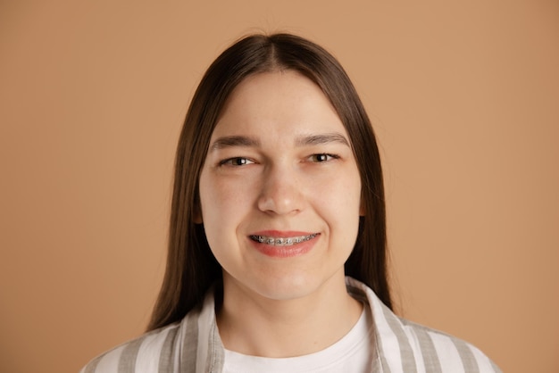 calm smiling girl with braces look at camera on studio beige background