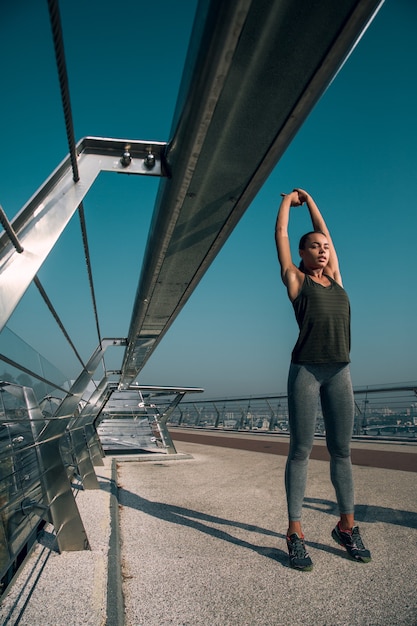 Calm sportswoman standing on tips of her toes and stretching hands up