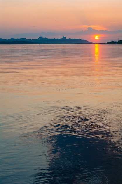 Calm water surface with pink sunset sky and sun through the clouds over Meditation water and sky