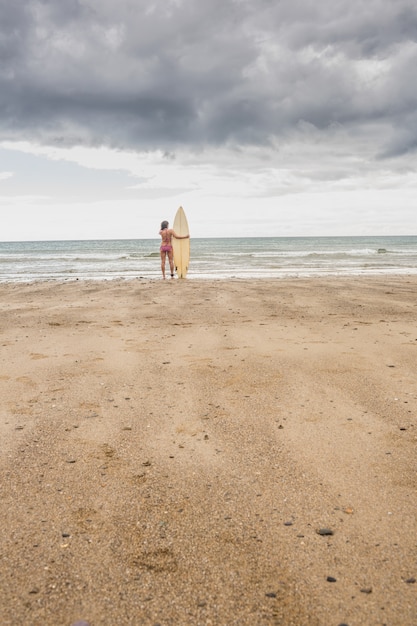 Foto donna calma in bikini con tavola da surf sulla spiaggia
