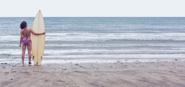 Calm woman in bikini with surfboard on beach