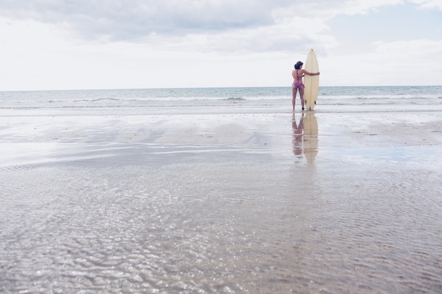 Calm woman in bikini with surfboard on beach