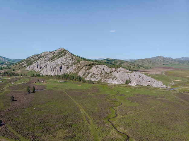 A calm and wonderful green natural drone lowland covered with a green clearing and a small rocky hill.