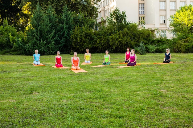 Allenamento di yoga calmo in un parco cittadino. gruppo di donne sedute in ginocchio con gli occhi chiusi