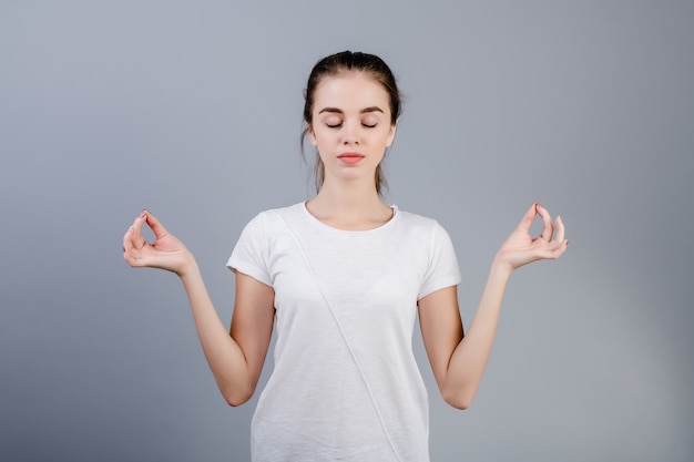 Calm young brunette woman relaxing and meditating isolated over grey