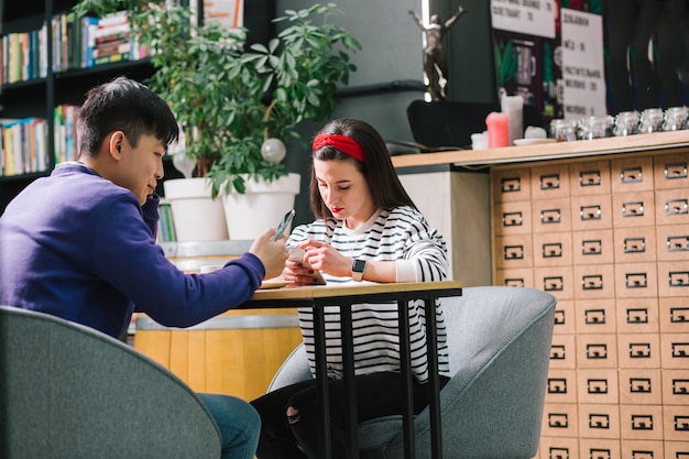 Photo calm young couple sitting in a cafe at the table and looking at the screens of their smartphones