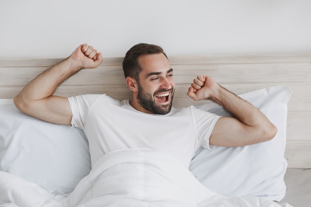 Calm young handsome bearded man lying in bed with white sheet pillow blanket in bedroom at home