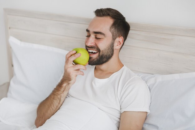 Calm young handsome bearded man lying in bed with white sheet pillow blanket in bedroom at home