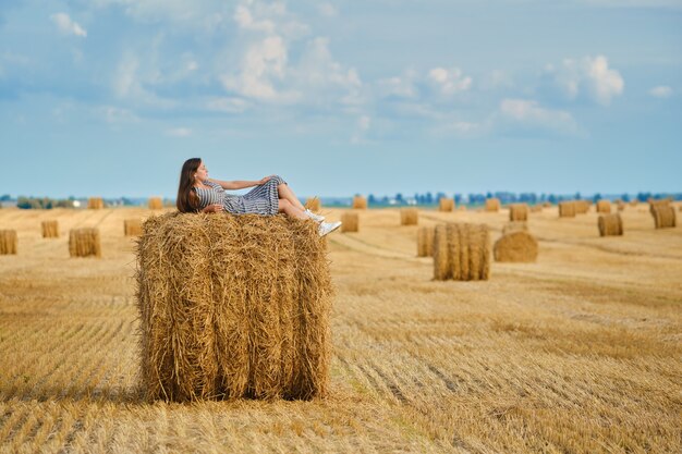Photo calm young woman laying on the top of stack of straw on the field