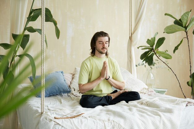 Uomo calmo in yoga sana sul letto e namaste, meditatore pacifico concentrato a casa la mattina