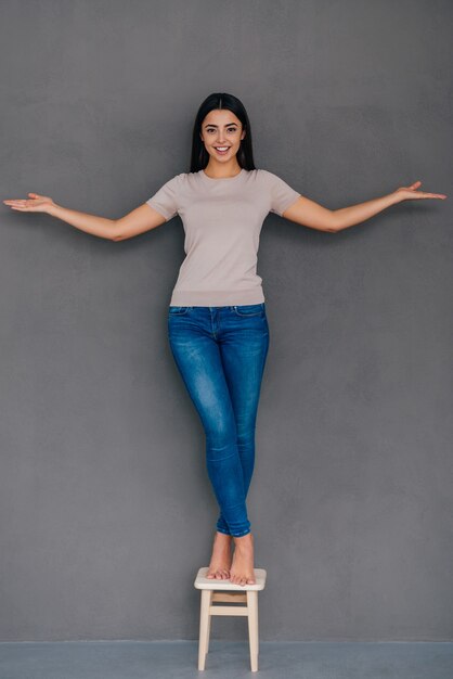 Calmness and balance. Beautiful young smiling woman balancing on chair and stretching out hands