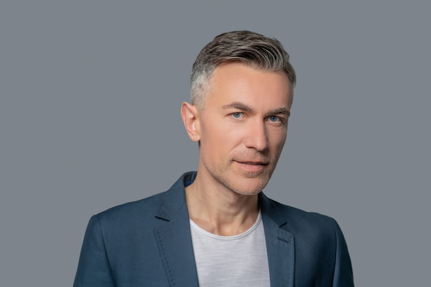 Calmness. Good looking middle aged man with gray eyes in jacket calmly looking at camera on background