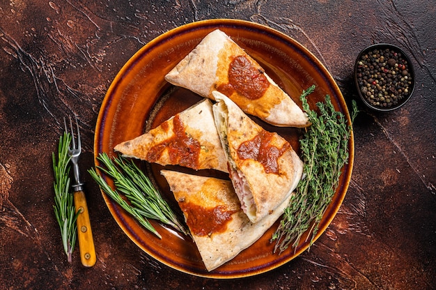 Calzone pizzastukken op rustieke plaat met tomatensaus en kruiden