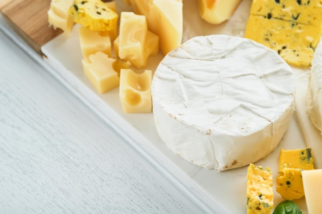 Camember and maasdam smoked cheese blue cheese parmesan brie cheese with basil and pepper on white marble board white wooden old background Set or assortment cheeses Top view Free copy space