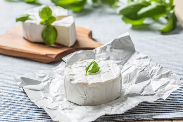 Camembert or brie cheese with basil leaves on table.