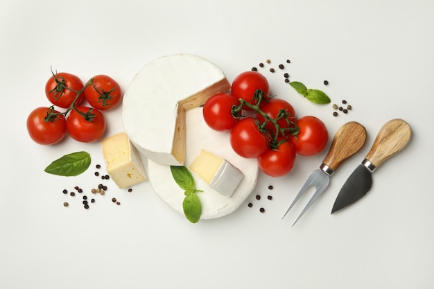 Camembert cheese, basil, tomato, knives and pepper on white background